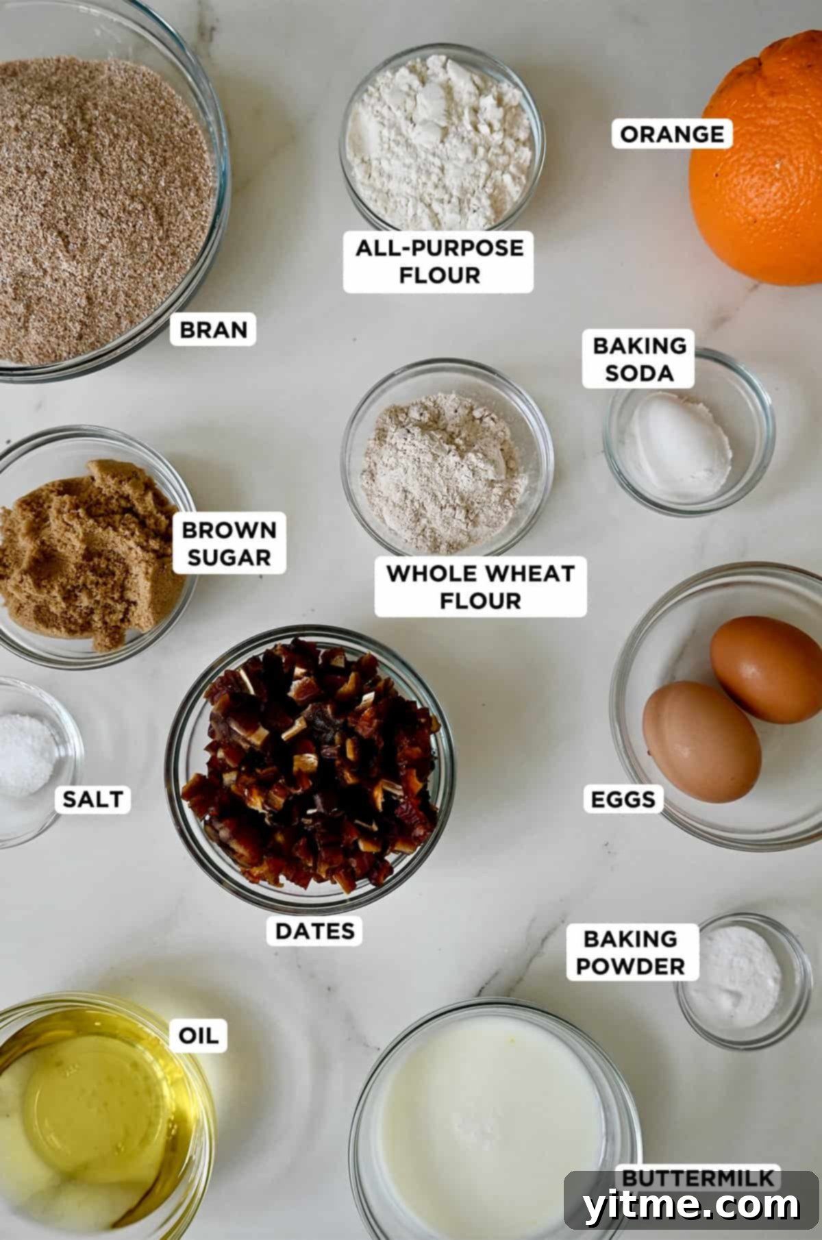 Various sizes of glass bowls containing ingredients ready to make bran muffins, including bran, dates, and flour.