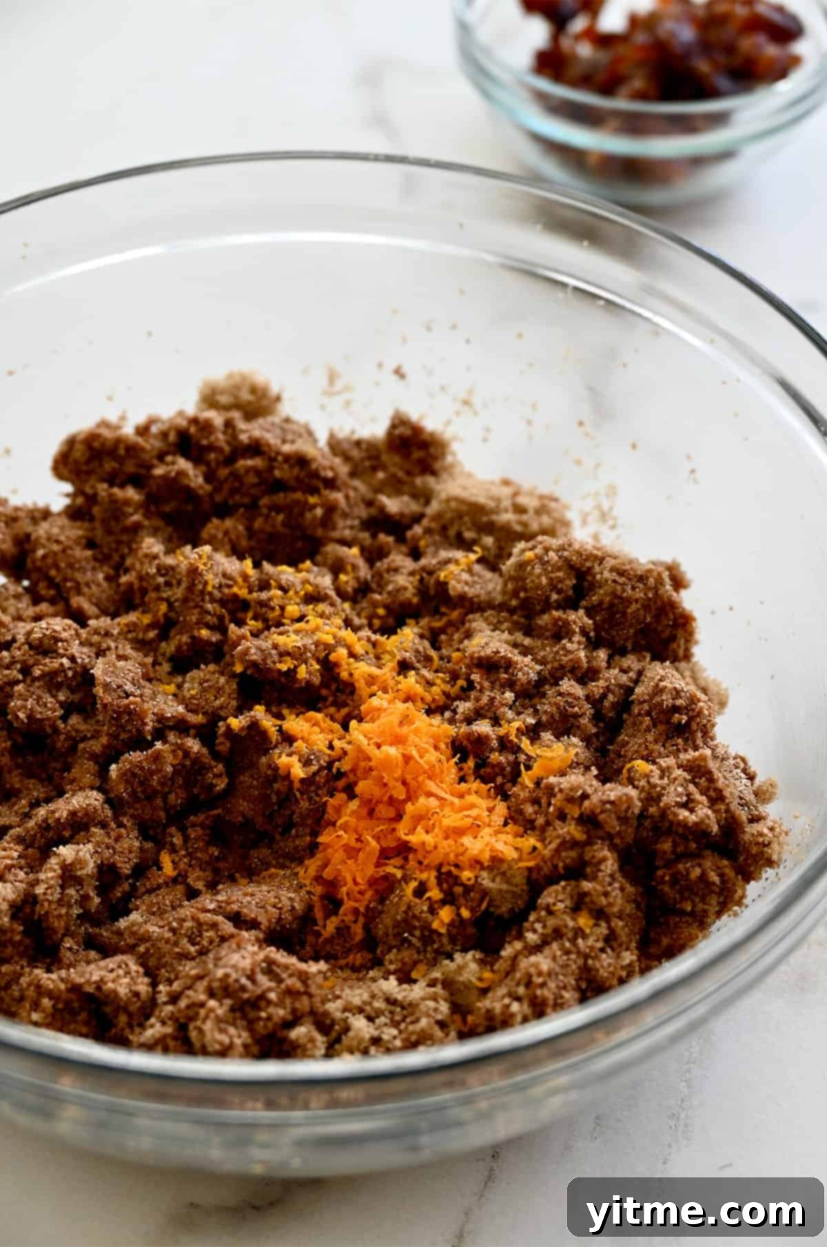 Orange zest being added atop bran muffin batter in a glass bowl.