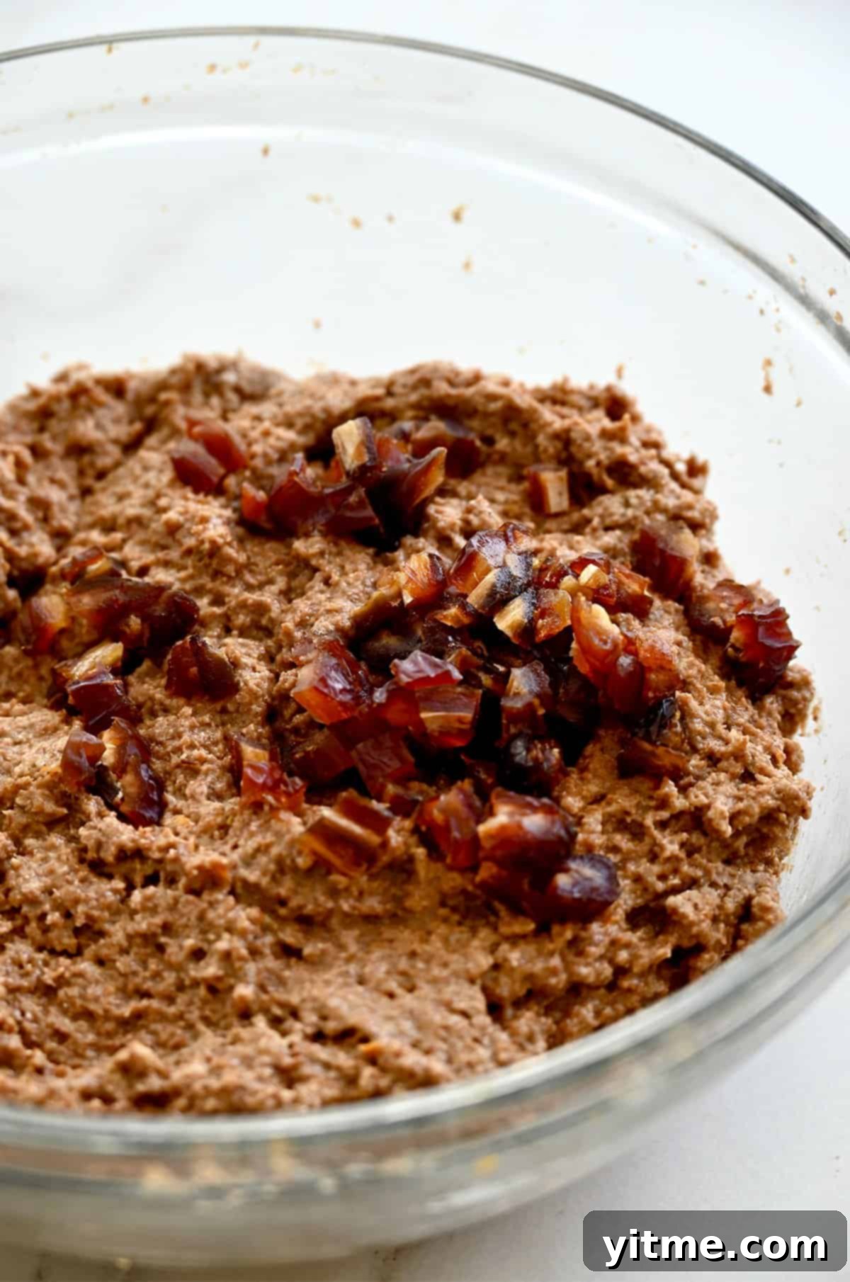 Chopped dates being folded into wheat bran muffin batter in a mixing bowl.