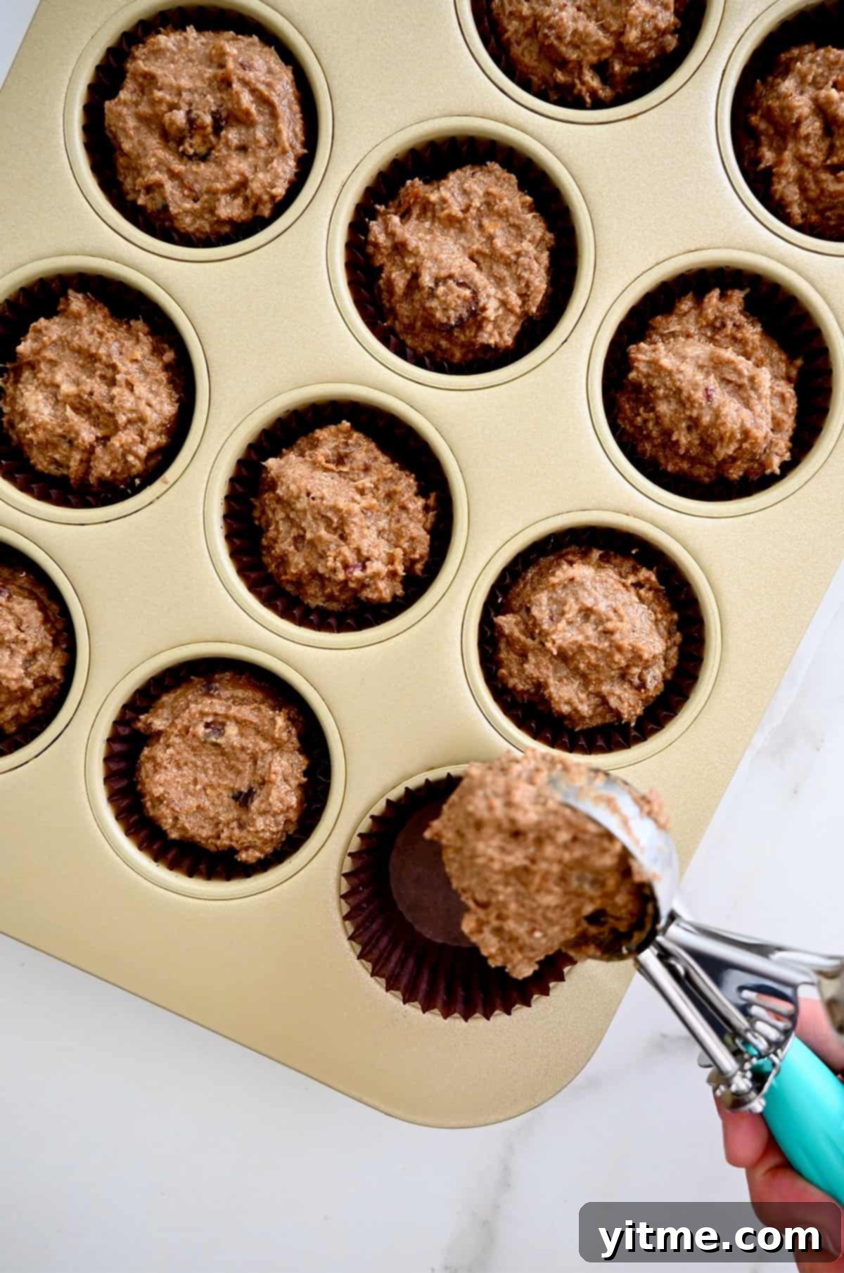 Scooping bran muffin batter into a paper-lined muffin tin.