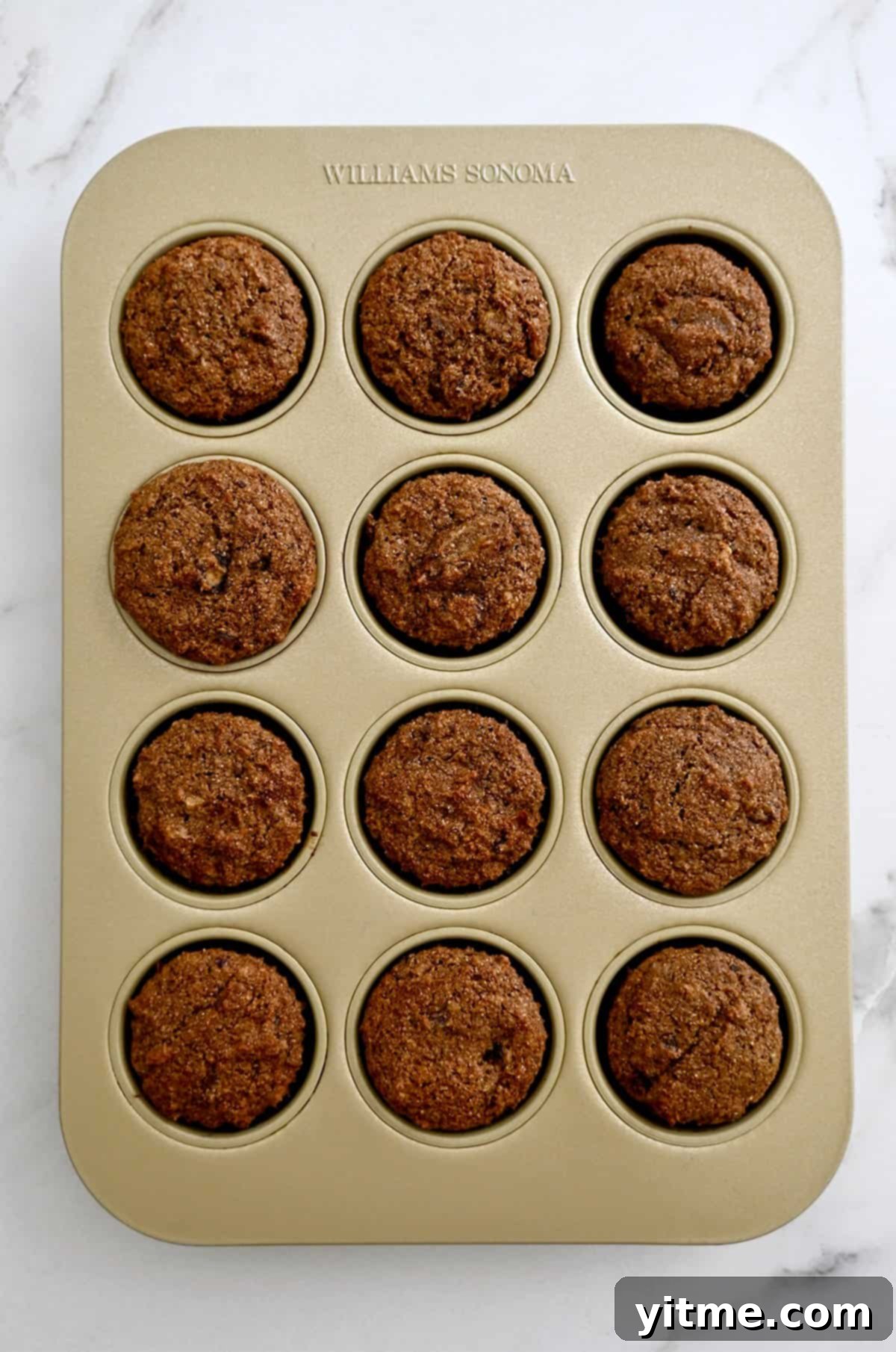 A tray of freshly baked bran muffins cooling in a 12-cup muffin tin.