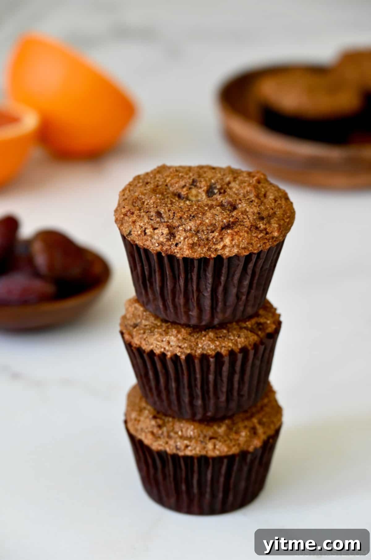 A stack of three healthy bran muffins, garnished with a sprinkle of orange zest, on a rustic surface.