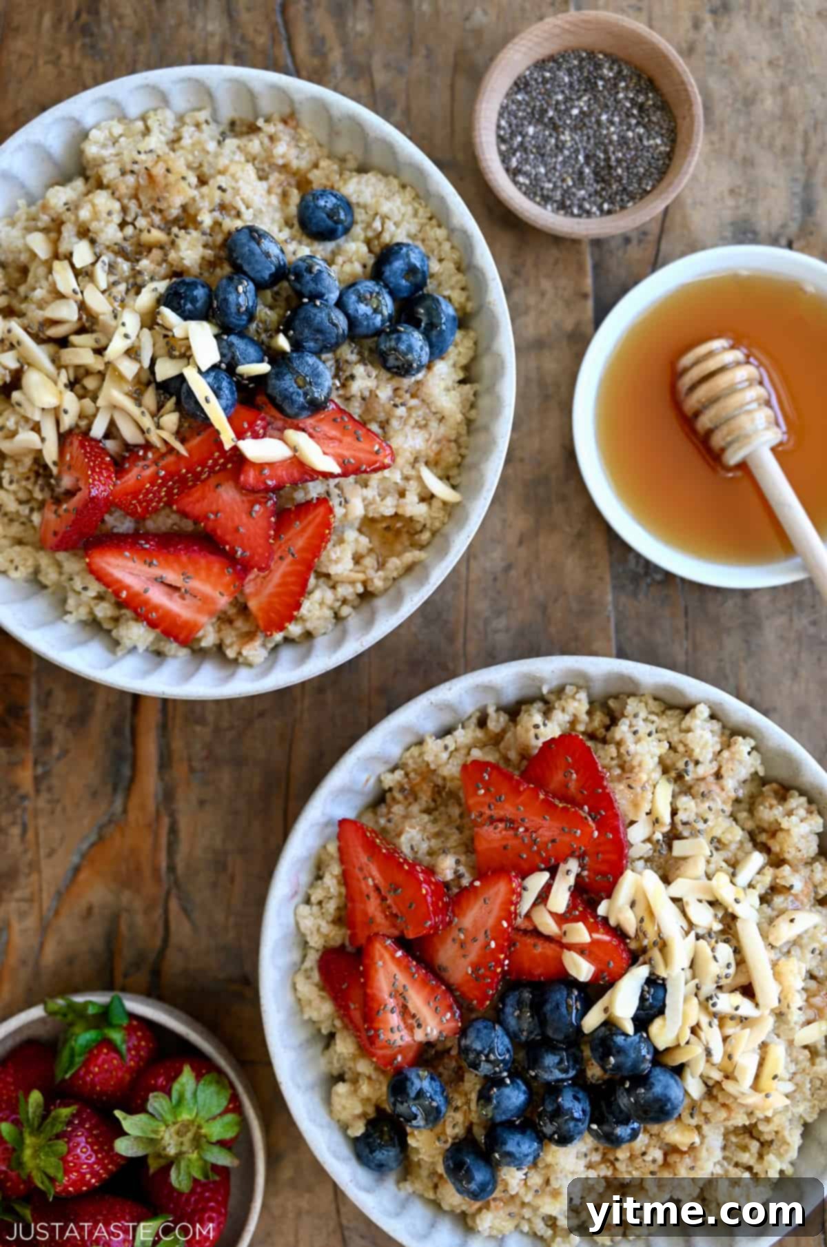 Two bowls containing creamy quinoa topped with fresh strawberries, blueberries, slivered almonds and chia seeds.