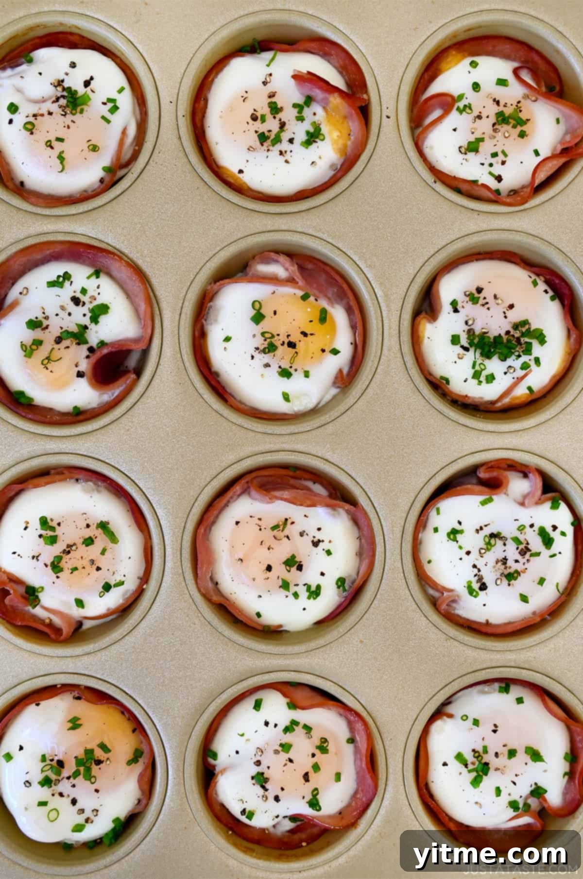 Baked ham and egg cups garnished with fresh chives in a muffin tin.