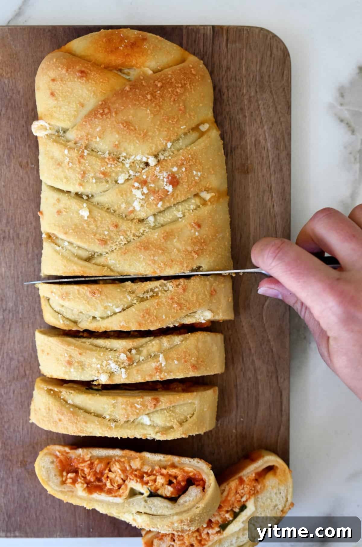 A hand holding a sharp knife cuts a chicken Stromboli into slices to serve.