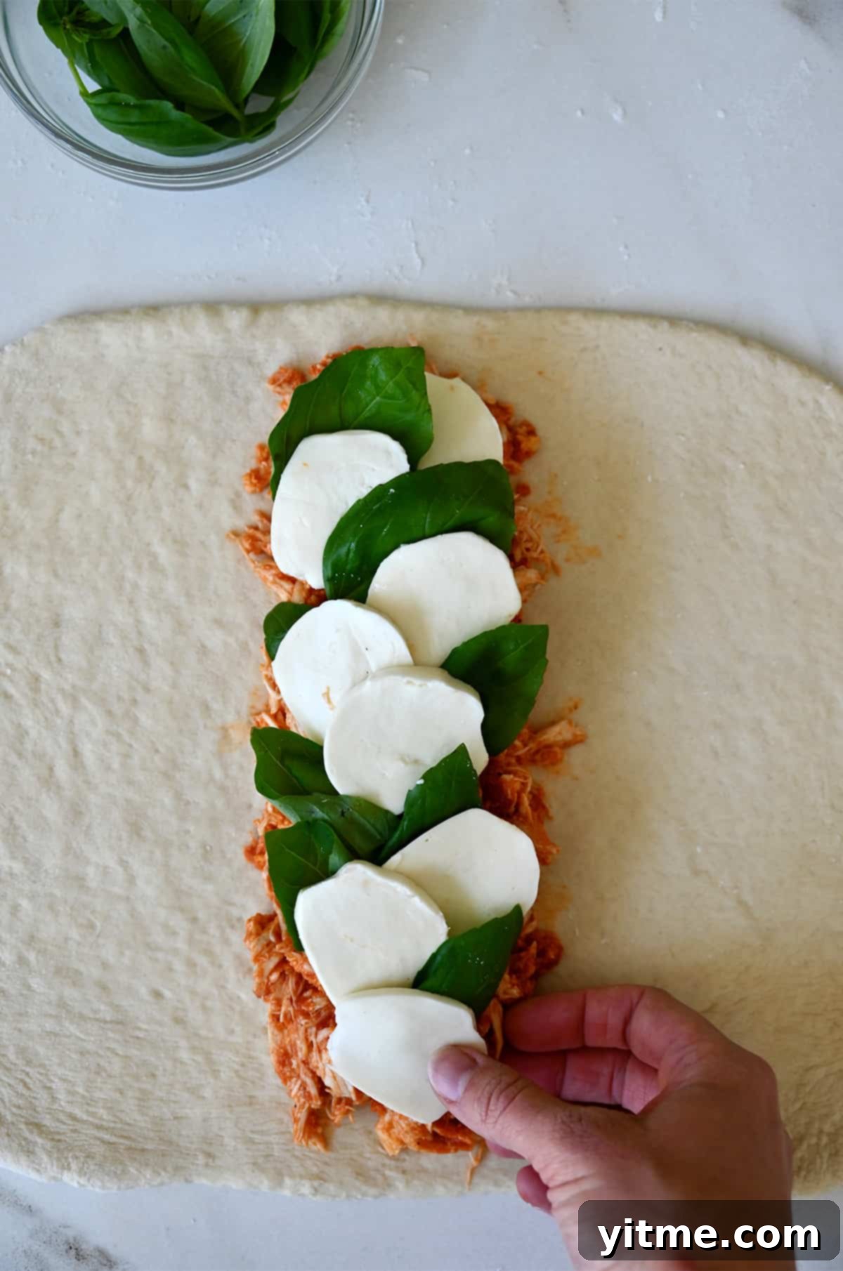 Pizza dough topped with shredded chicken, mozzarella slices and basil leaves.