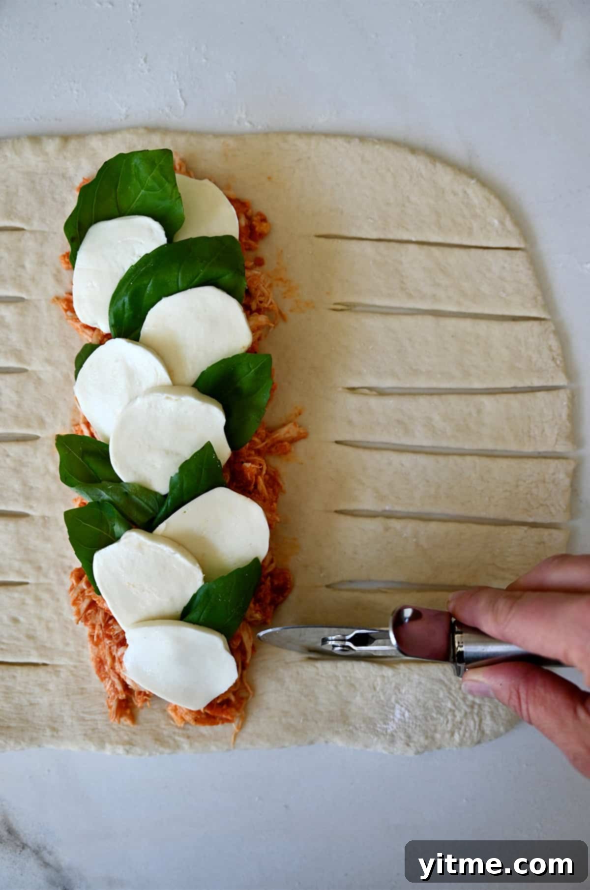 A hand holding a pizza wheel cuts slits into dough topped with Stromboli fillings.