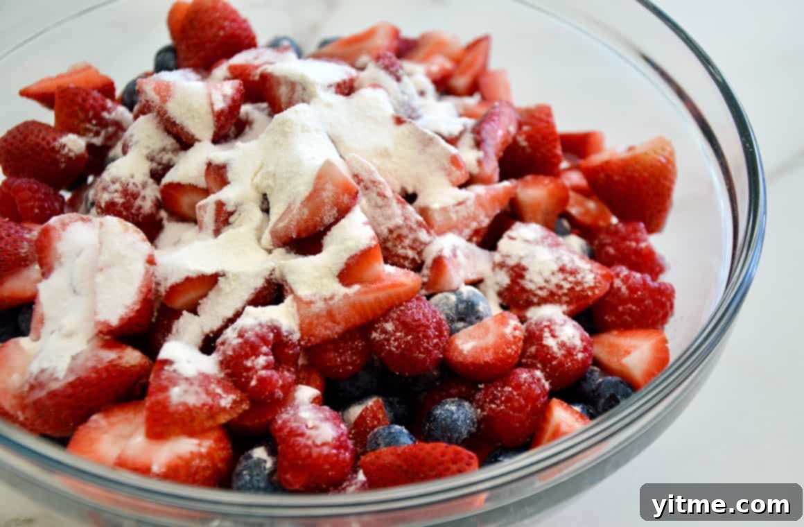 Fresh strawberries, raspberries, and blueberries in a glass bowl with flour