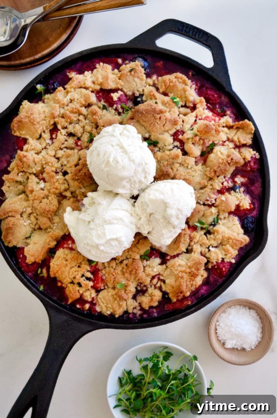 A cast-iron skillet with fruit crumble topped with ice cream