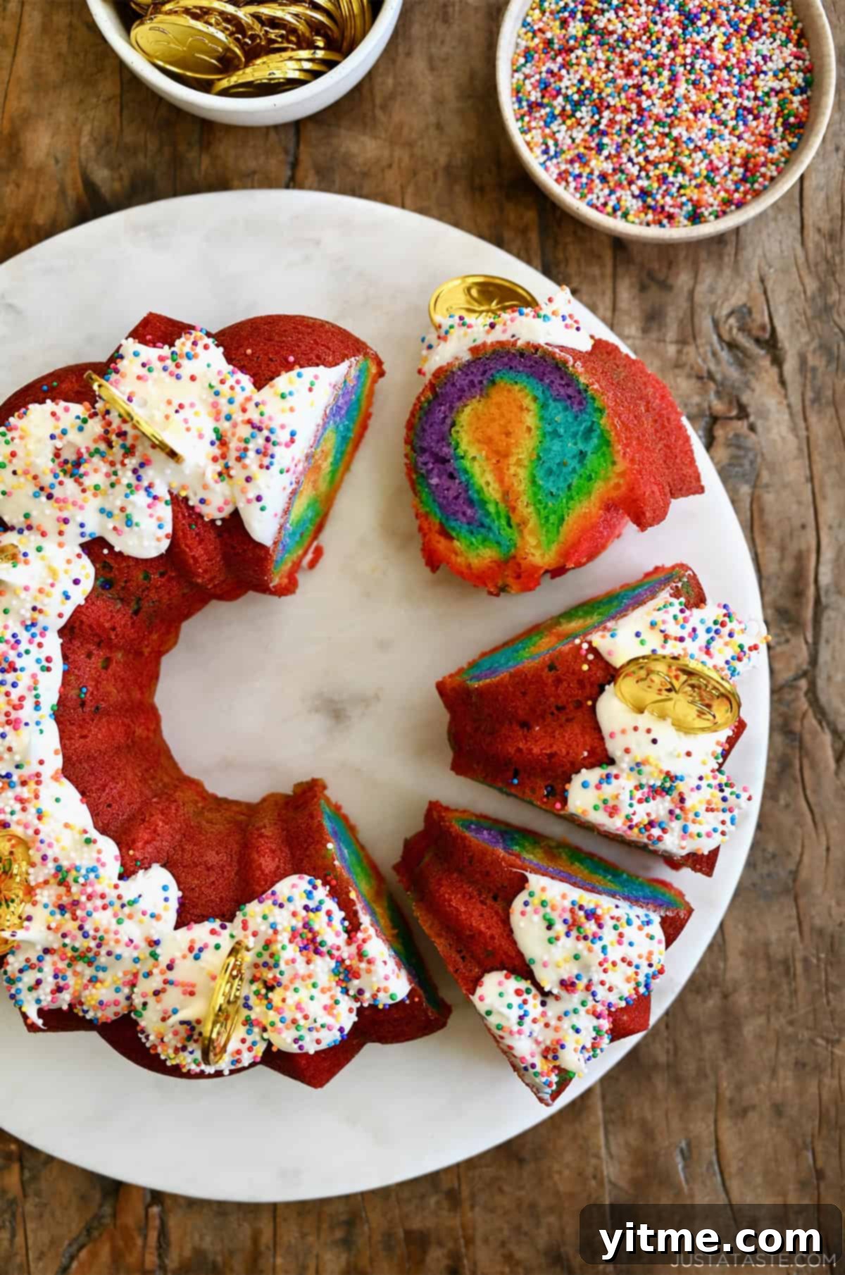 Slices of rainbow cake with vanilla frosting and rainbow sprinkles on a cake serving plate, showcasing vibrant layered colors.