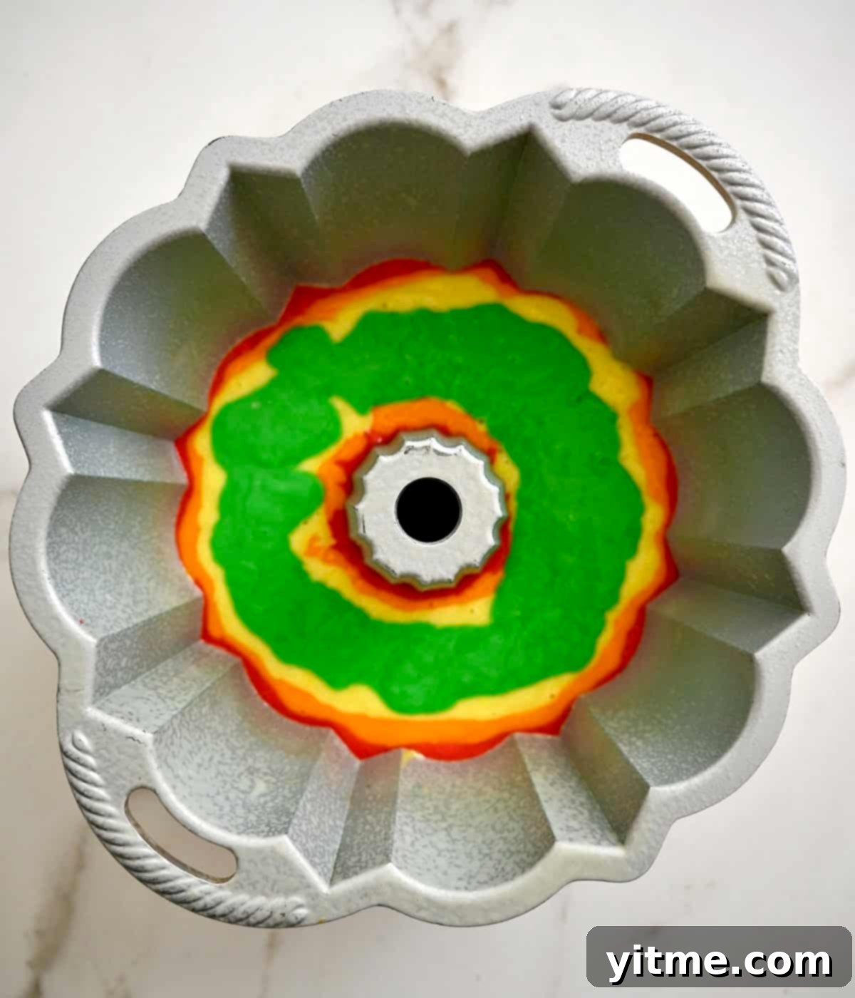 Green cake layer in a bundt pan, added without disturbing the previous layers of yellow, orange, and red.