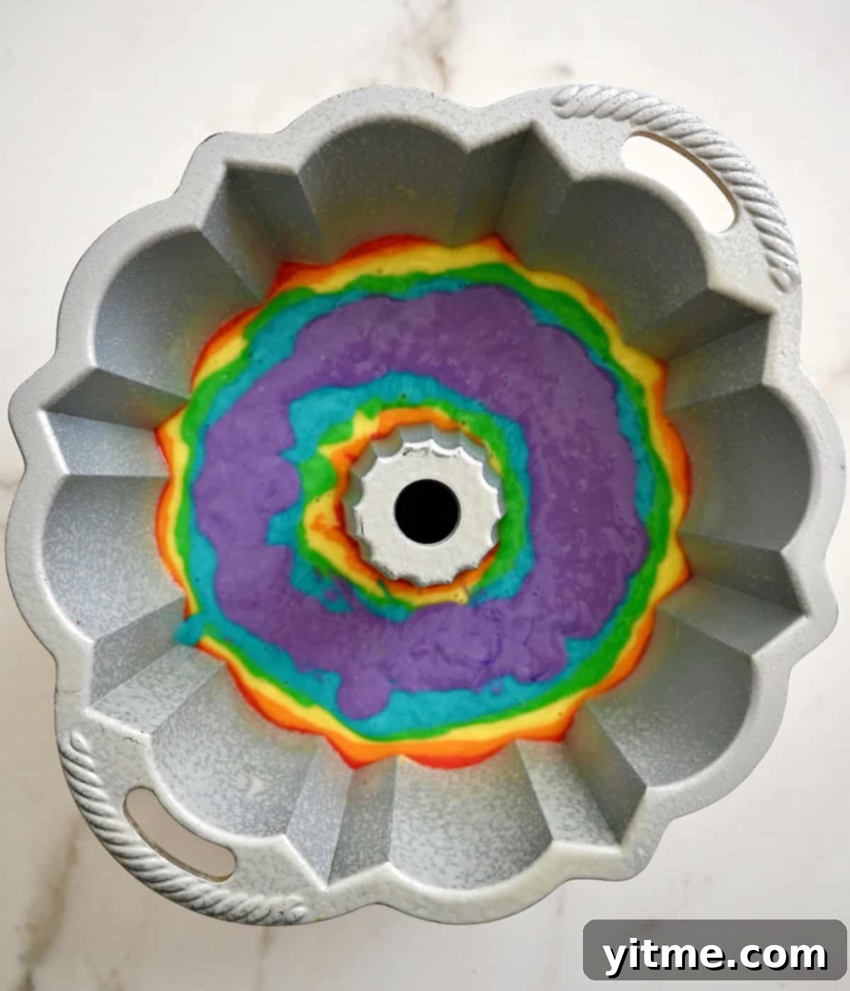 A bundt pan containing all six layers of a rainbow cake: red, orange, yellow, green, blue and purple, ready for baking.