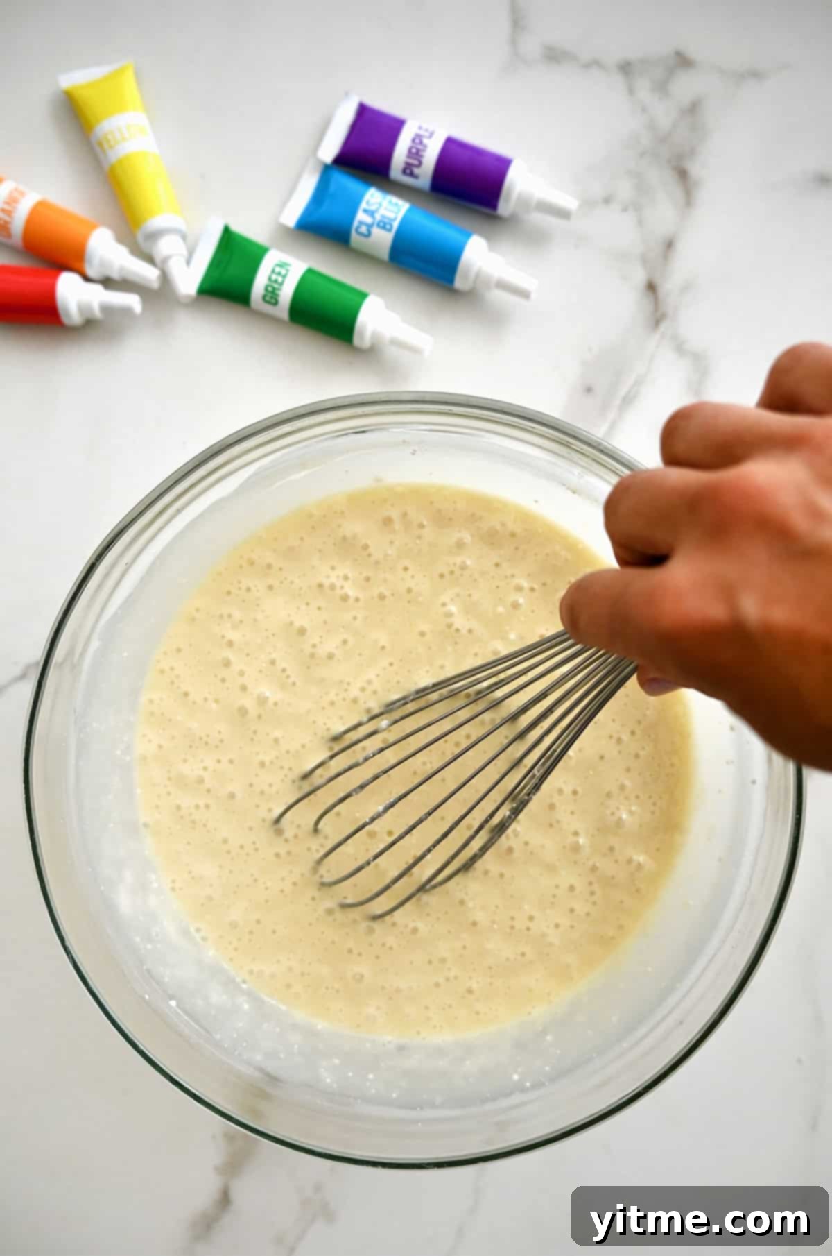 Cake mix batter in a large bowl with tubes of gel food coloring nearby, ready for dyeing.