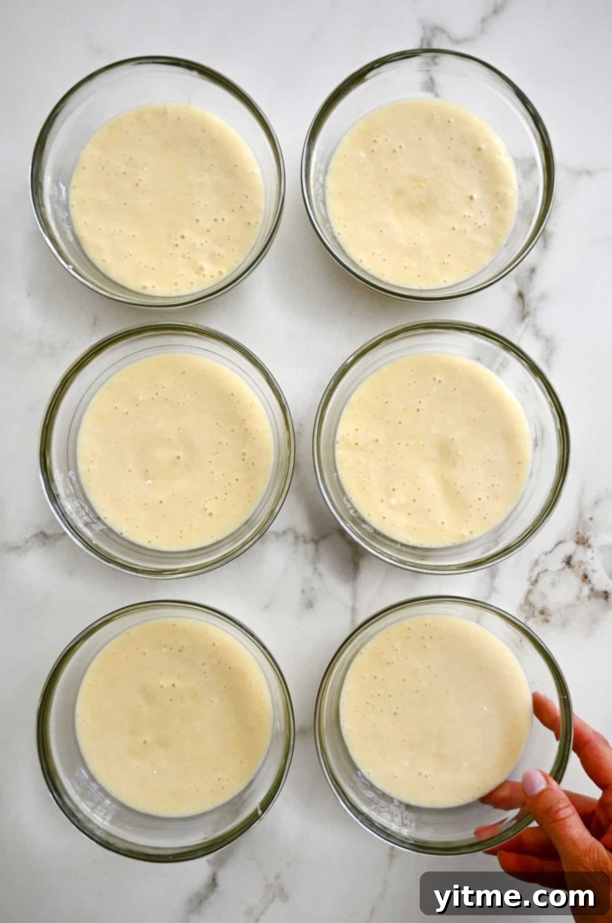 Six bowls containing evenly divided cake batter, ready for coloring.