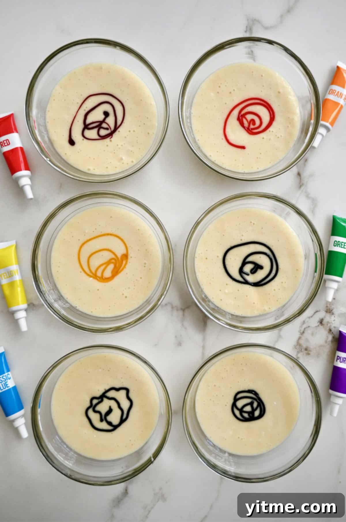 Adding gel food coloring to small bowls containing cake batter, illustrating the dyeing process.