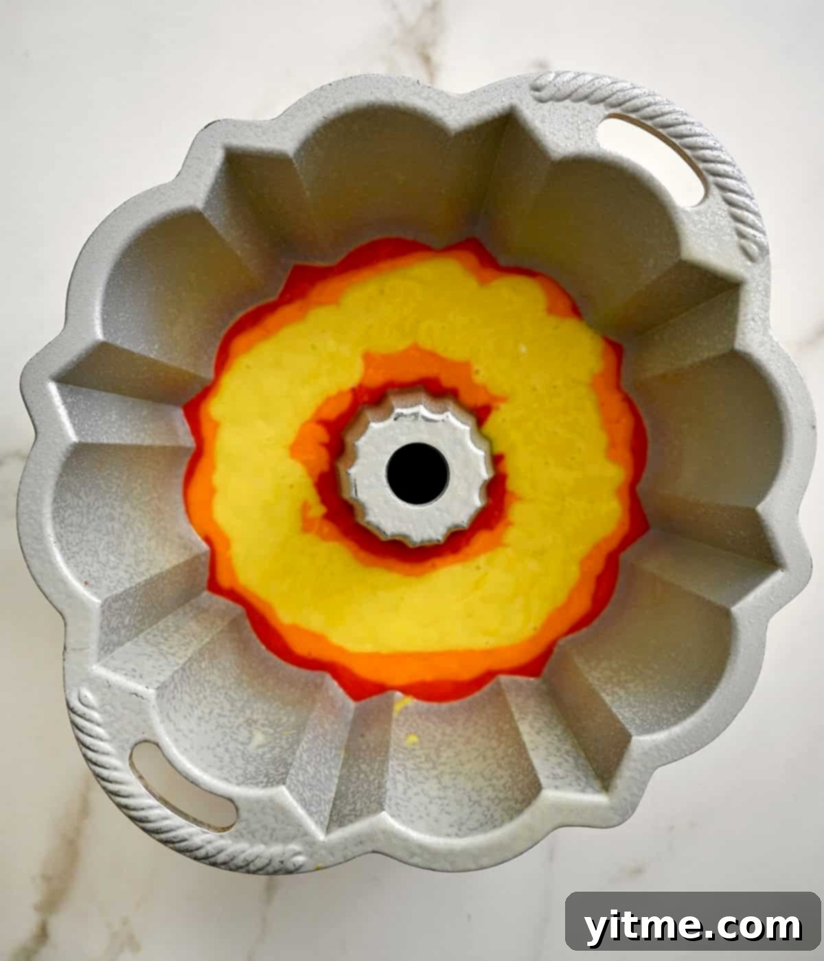 Yellow cake batter layered precisely above the orange layer in a rainbow bundt cake, showcasing the layering method.