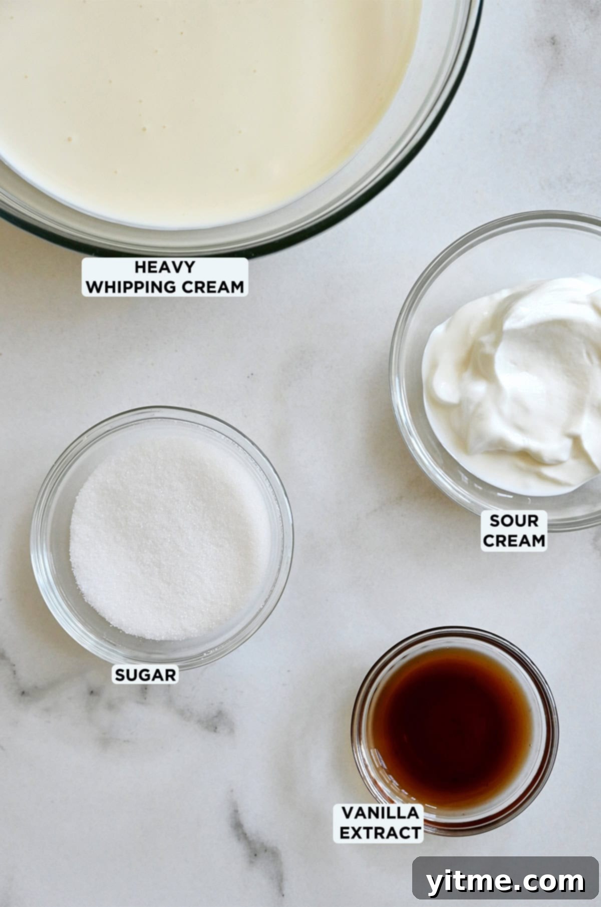 Glass bowls containing heavy cream, sour cream, sugar and vanilla extract, ready to be combined for making whipped cream.