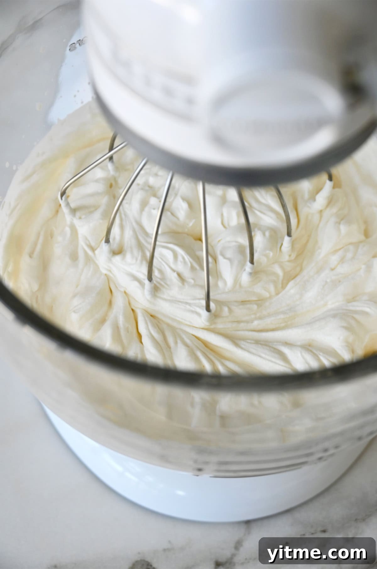 Heavy whipping cream and sour cream being whipped together in a stand mixer bowl with the whisk attachment, showing the early stages of whipping.
