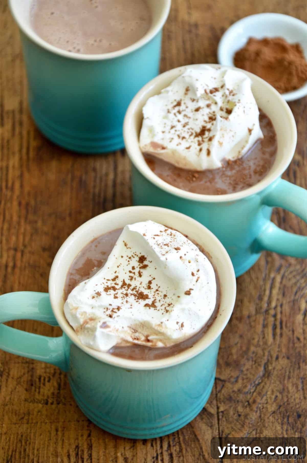 Two mugs with hot cocoa topped with a generous dollop of sweet and tangy homemade whipped cream, ready to be enjoyed.
