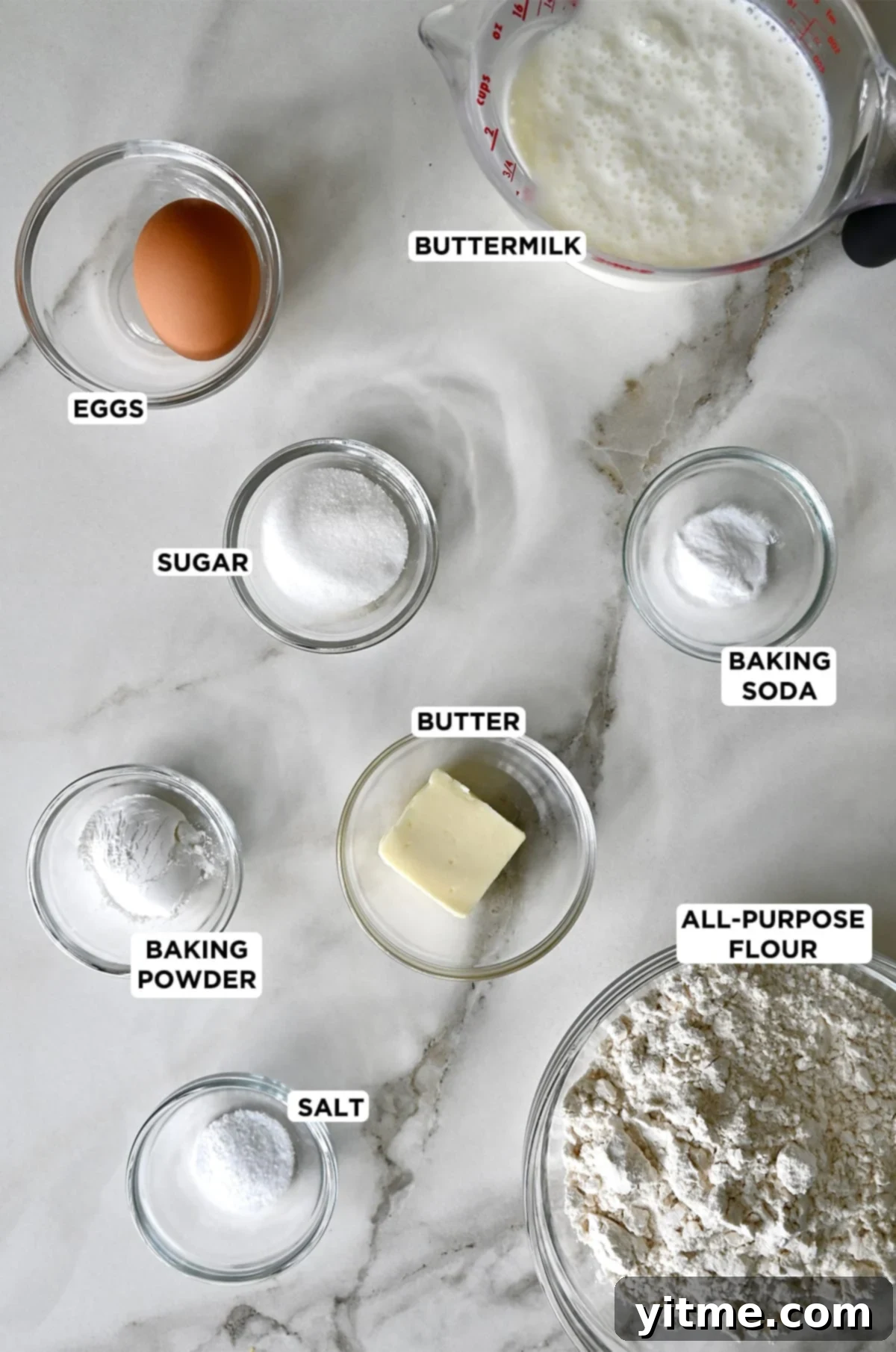 Various sizes of glass bowls containing these ingredients: buttermilk, baking soda, all-purpose flour, butter, salt, baking powder, sugar and a whole egg.