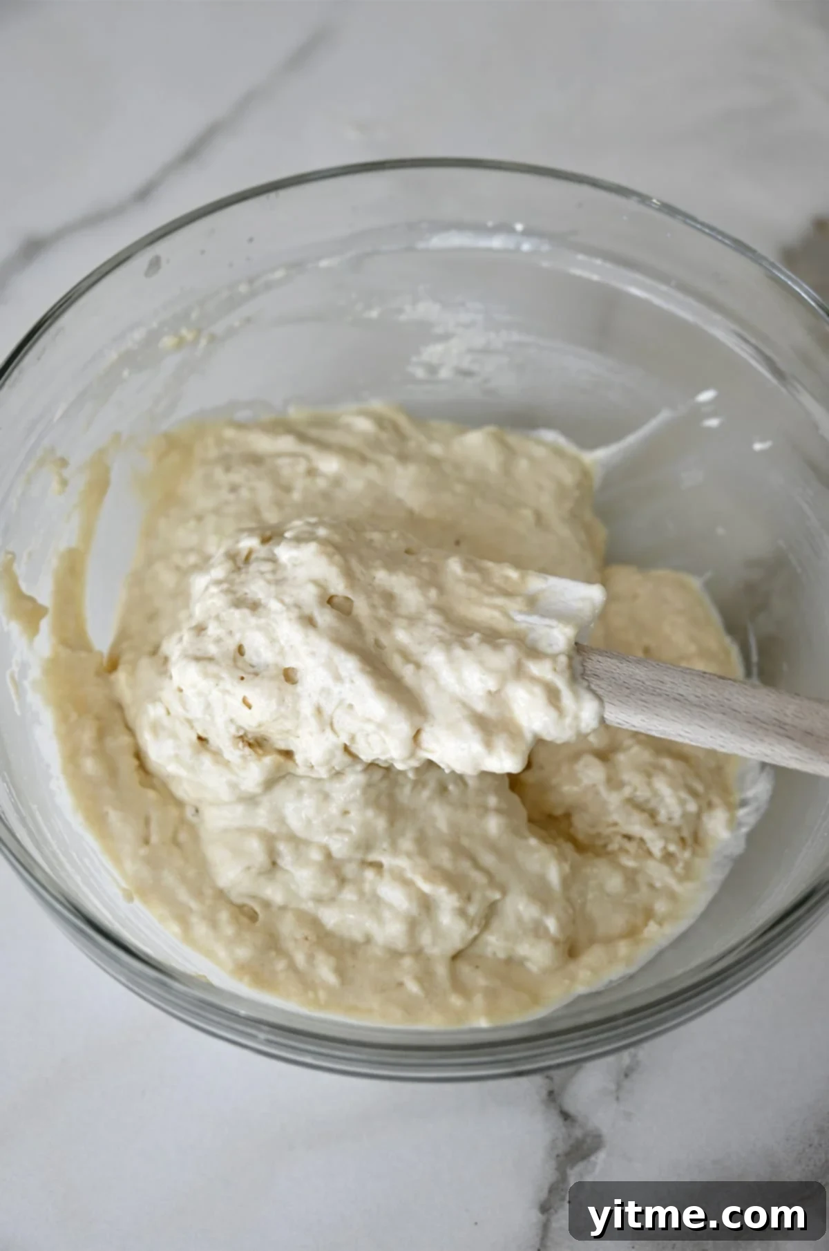 Thick buttermilk pancake batter in a glass bowl with a spatula.