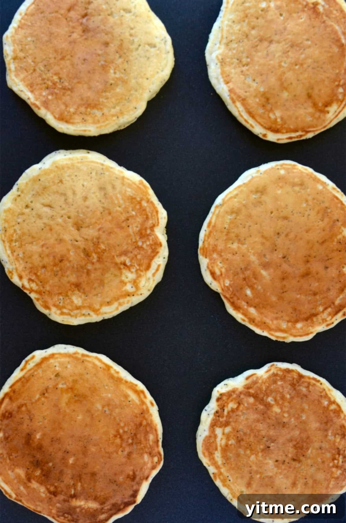Two rows of golden brown pancakes on a griddle.
