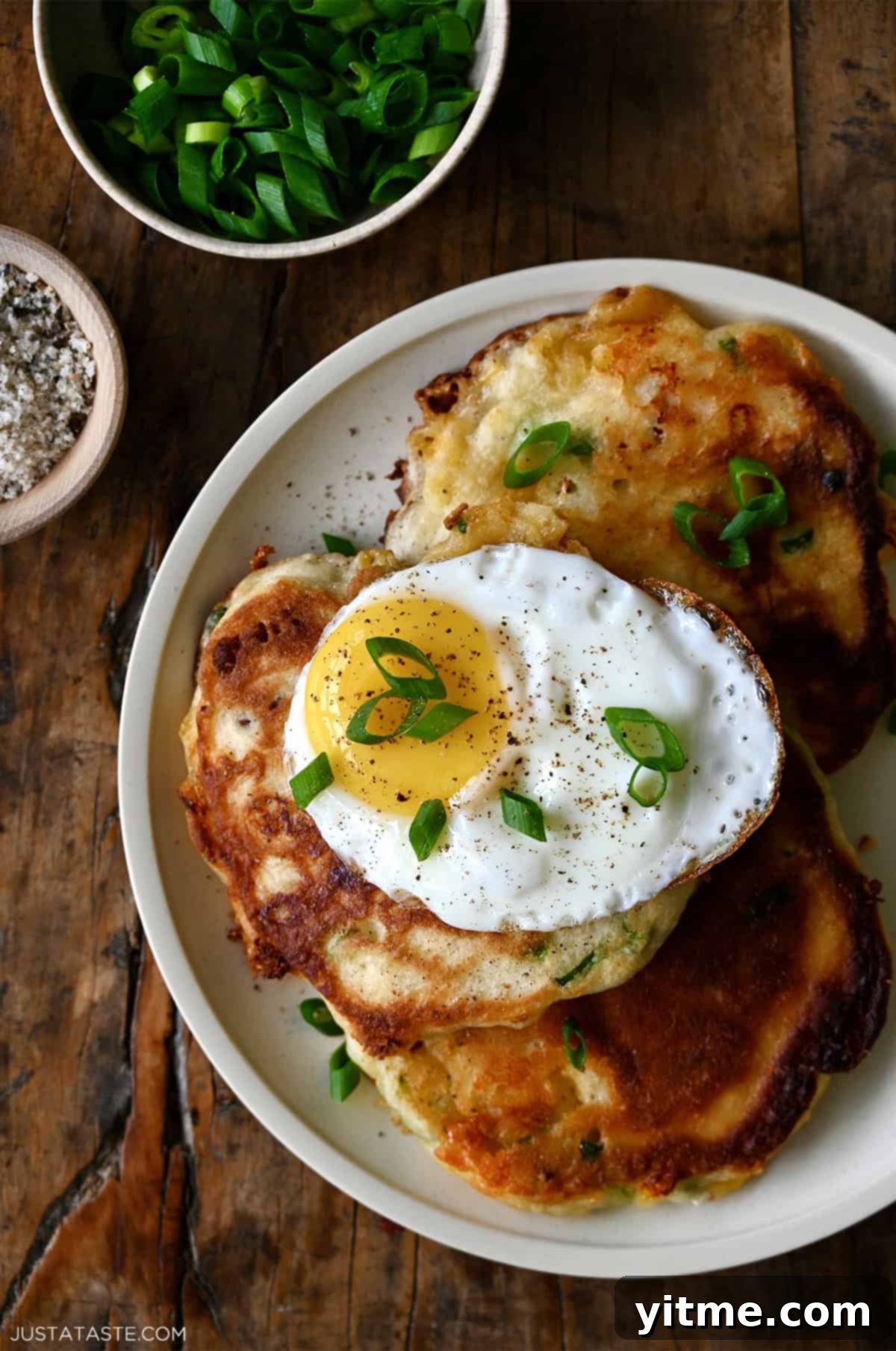 Savory pancakes with bacon and cheese topped with a fried egg and sliced scallions.