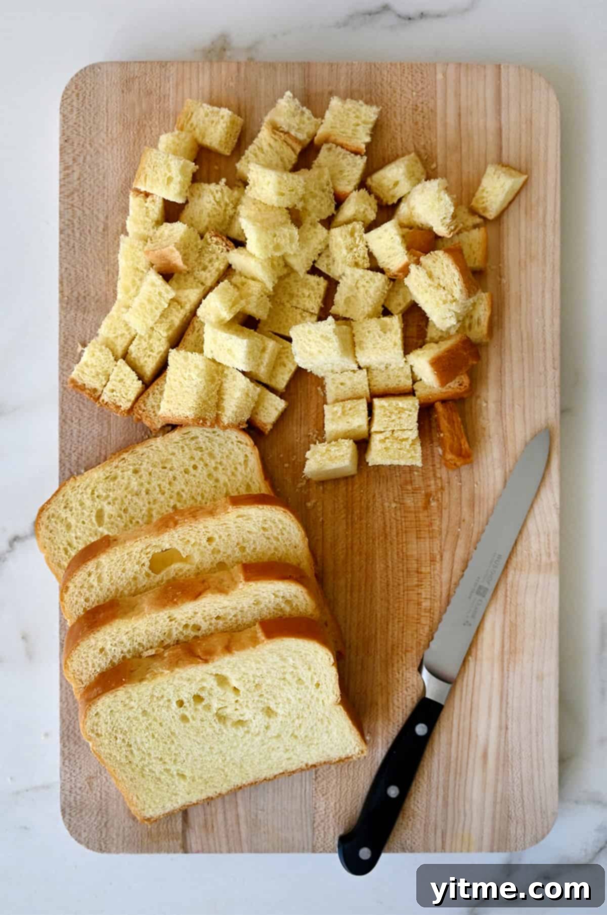 Cinnamon-Swirl French Toast Bites 4 Diced brioche next to four slices of brioche and a sharp knife on a wood cutting board.