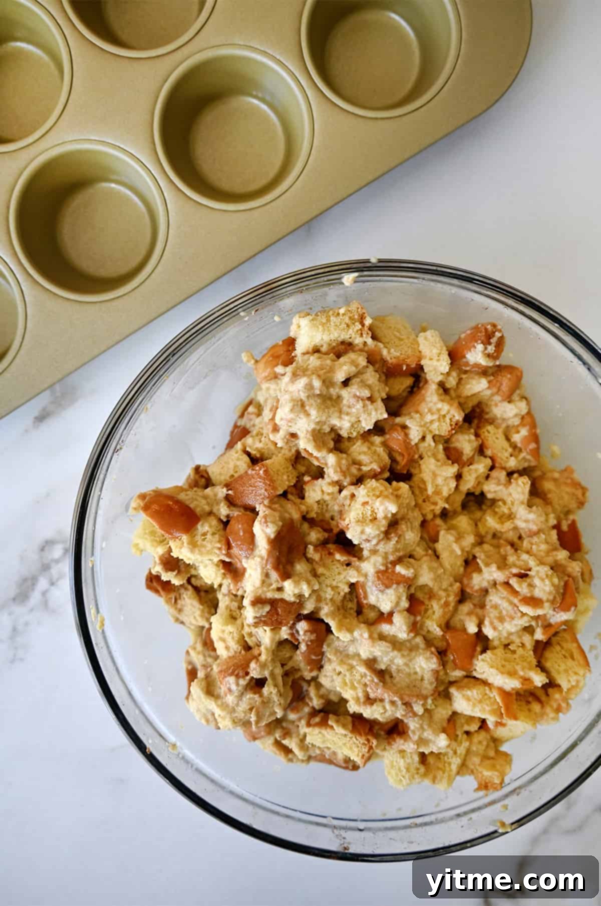 Cinnamon-Swirl French Toast Bites 5 Bread cubes soaked in a vanilla custard in a clear bowl next to a muffin pan.