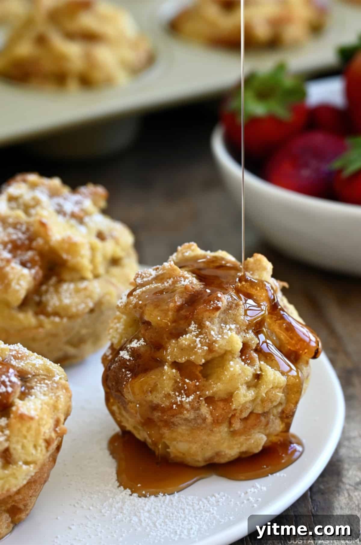Cinnamon-Swirl French Toast Bites 7 Maple syrup being drizzled atop a cinnamon French toast muffin on a white plate with two more French toast cups.
