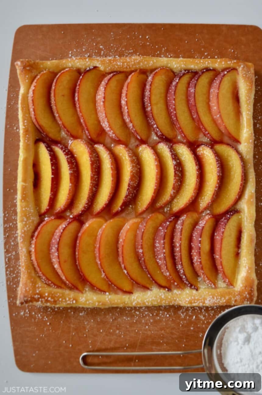 Overhead view of a 5-Ingredient Peach Tart with sliced peaches and powdered sugar on a puff pastry crust.