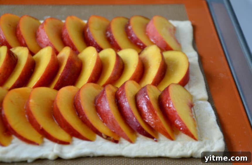 Puff pastry topped with rows of fresh peach slices ready to be baked into a 5-Ingredient Peach Tart.
