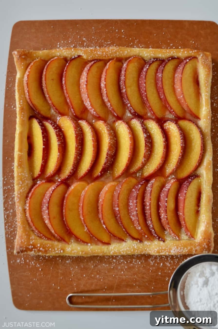 Overhead view of a 5-Ingredient Peach Tart with sliced peaches and powdered sugar on a puff pastry crust.