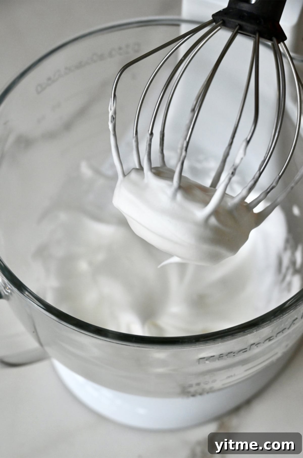 Whipped egg whites in the bowl of a stand mixer.