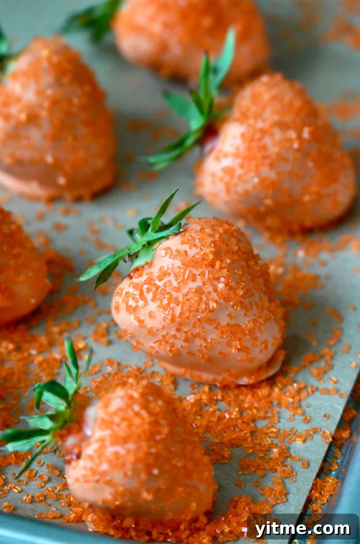 Strawberries dipped in orange candy melts on a baking sheet.