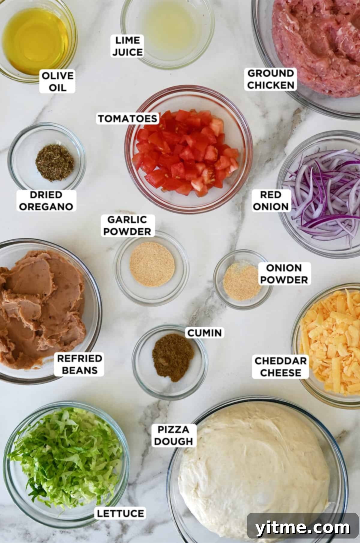 Ingredients for taco pizza including pizza dough, ground chicken, refried beans, cheese, lettuce, tomatoes, and taco seasoning.