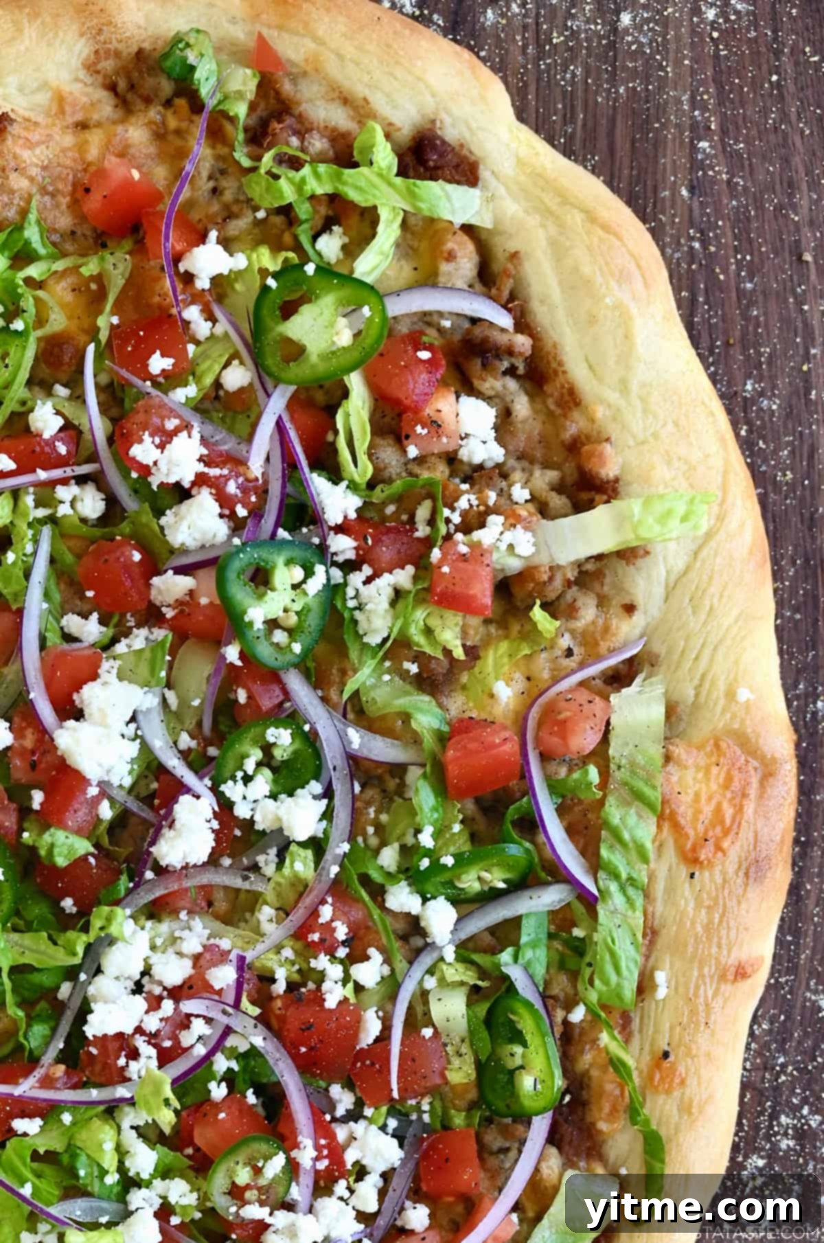Close up of cheesy chicken taco pizza with fresh toppings, including lettuce, tomatoes, jalapeños, and cheese.
