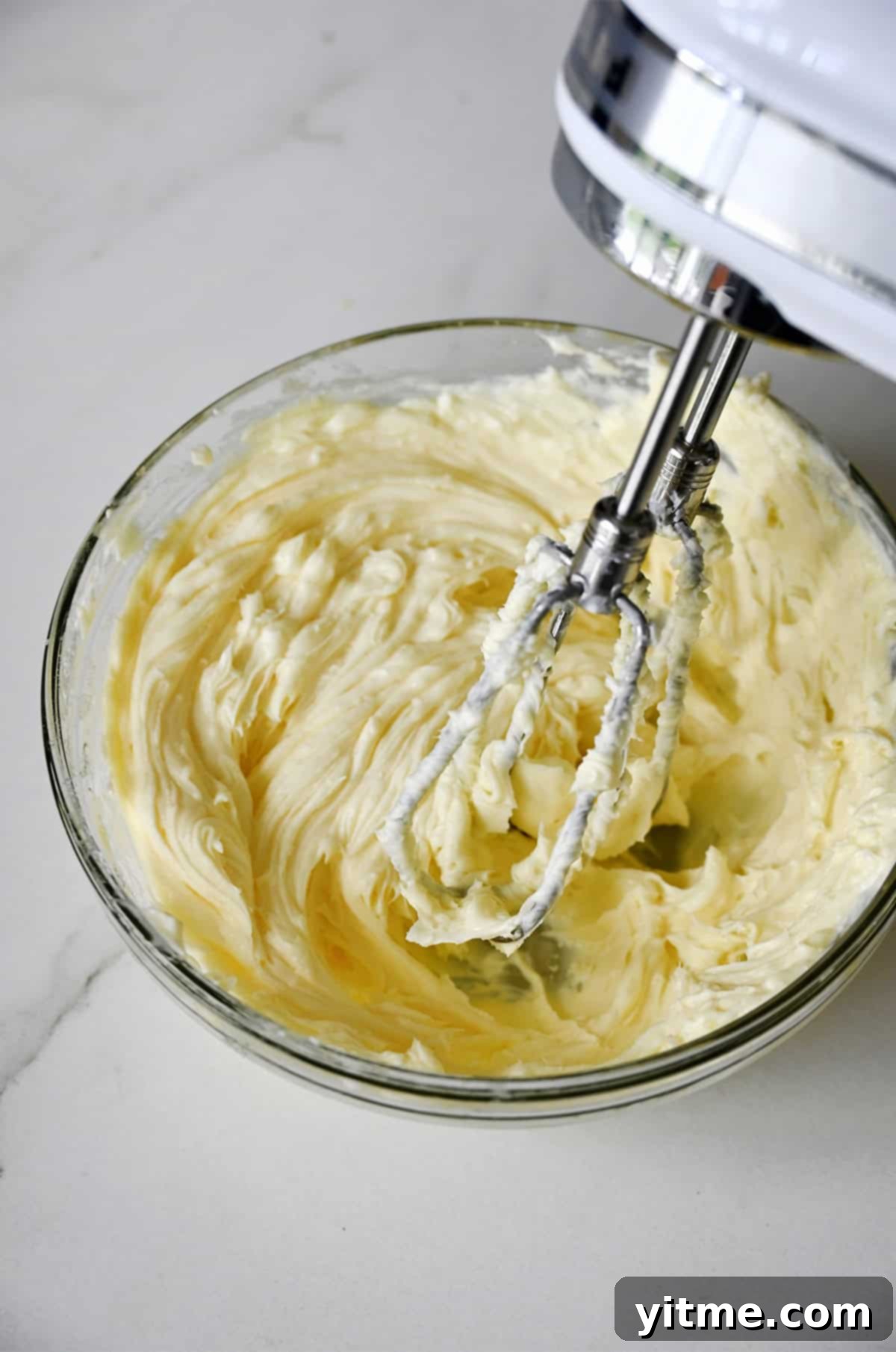 Cheesecake filling in a glass bowl with a hand mixer hovering over the top.