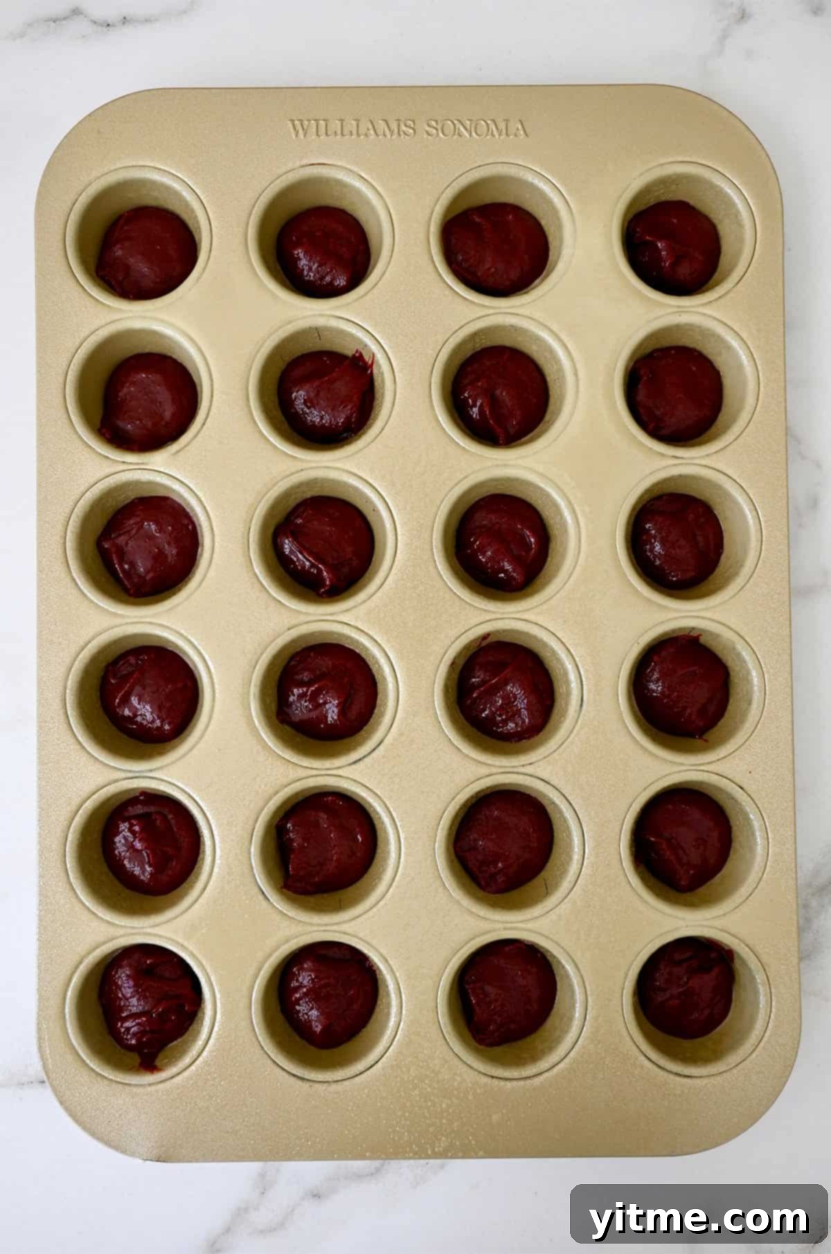 A mini muffin tin containing red velvet brownie batter.