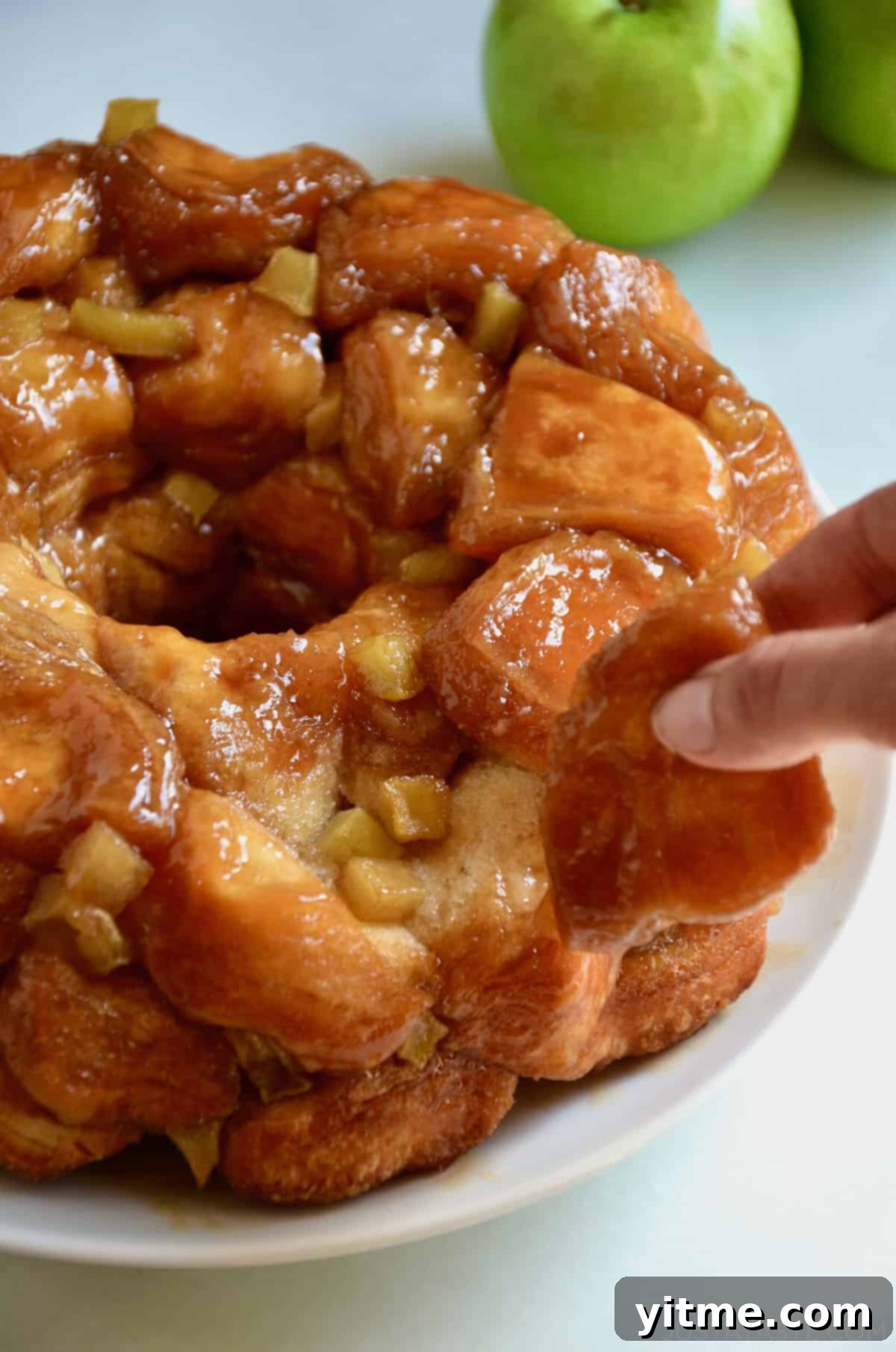 A close-up shot of a hand pulling apart a piece of caramel apple monkey bread, showcasing the gooey caramel and tender biscuit layers.