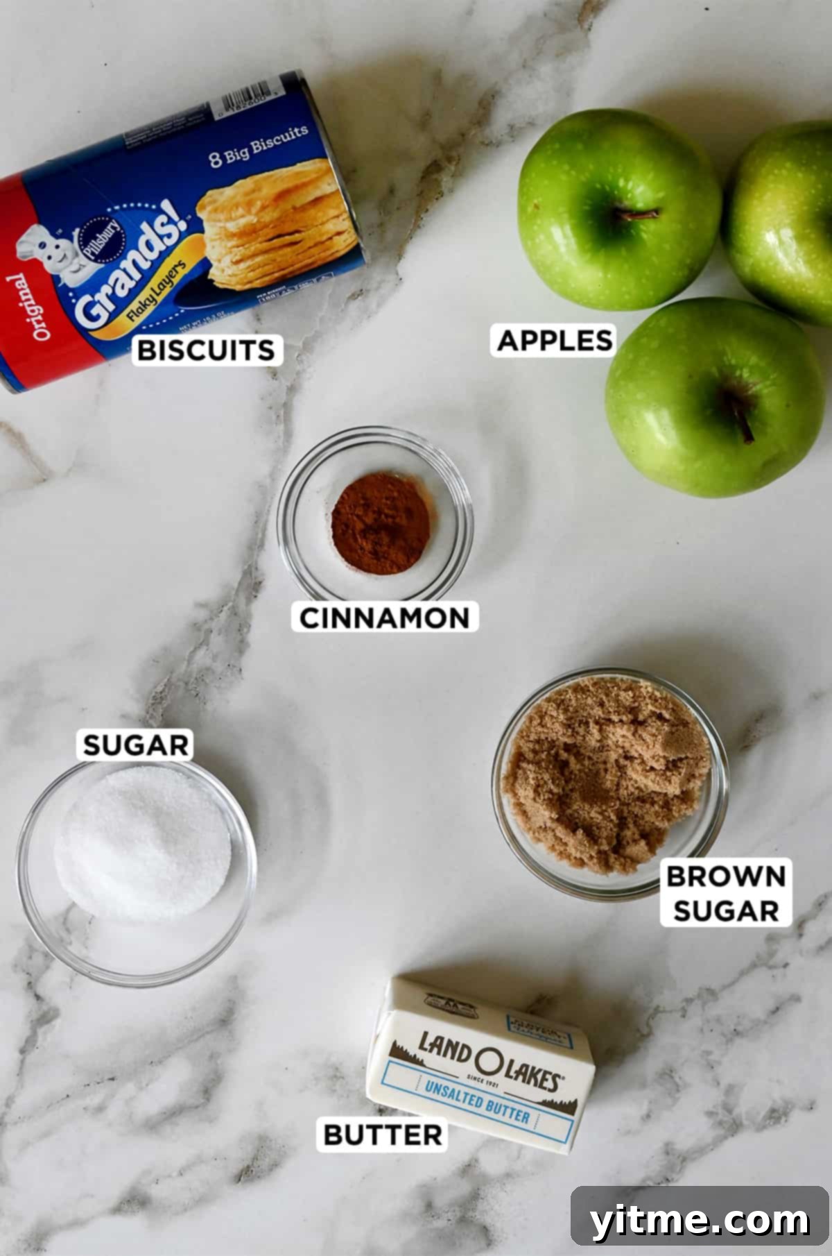 An arrangement showcasing the key ingredients for Caramel Apple Monkey Bread: Pillsbury refrigerated biscuits, Granny Smith apples, brown sugar, ground cinnamon, sugar, and butter.