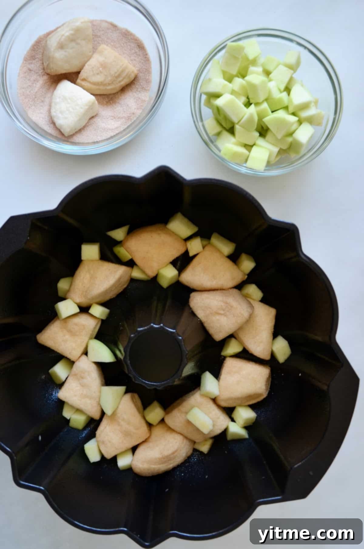 A greased bundt pan filled with layers of diced Granny Smith apples and pieces of cinnamon-sugar coated canned biscuit dough.