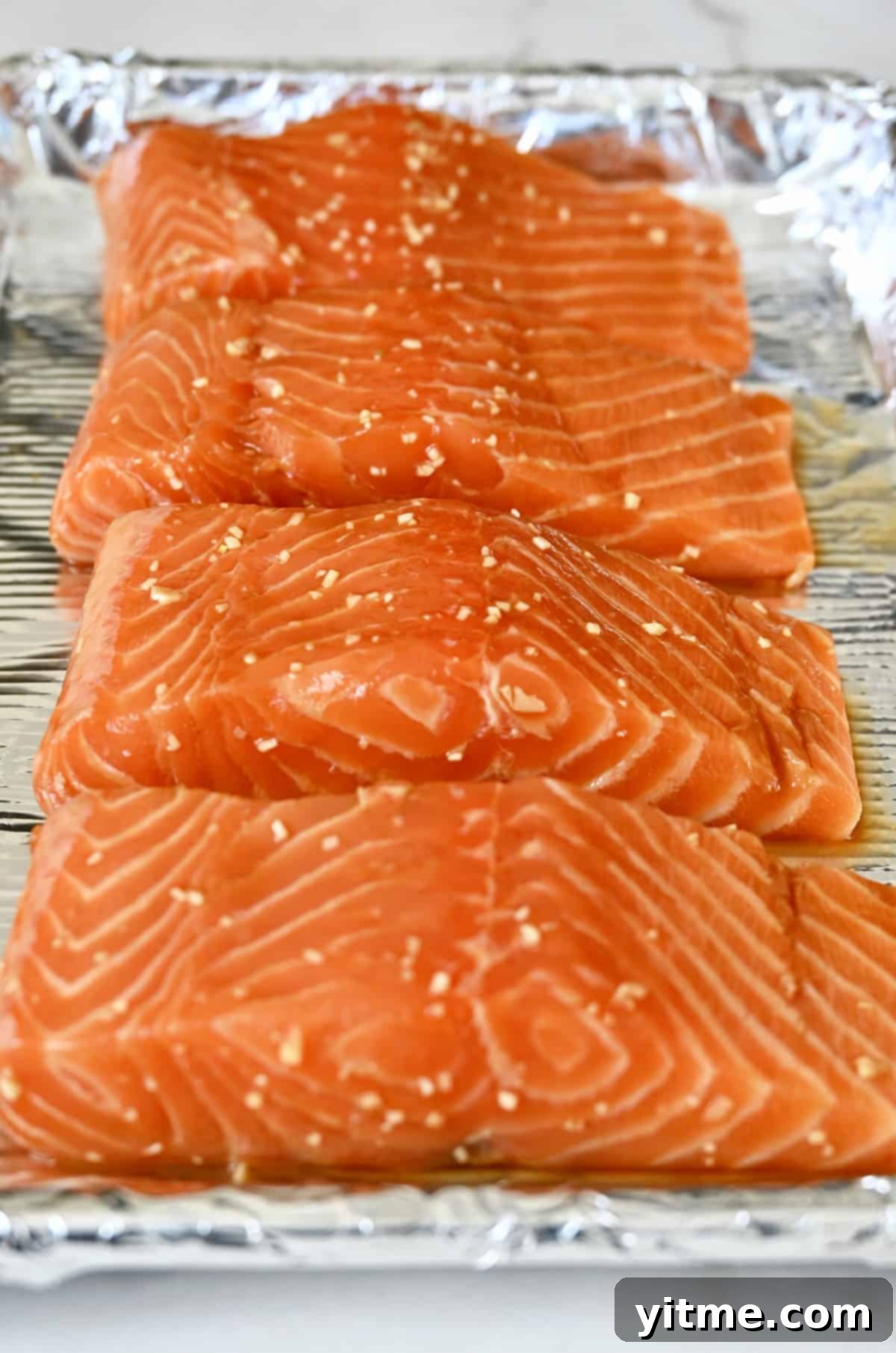 Honey-Garlic Glazed Salmon Delight 6 Marinated salmon on a baking sheet lined with aluminum foil.