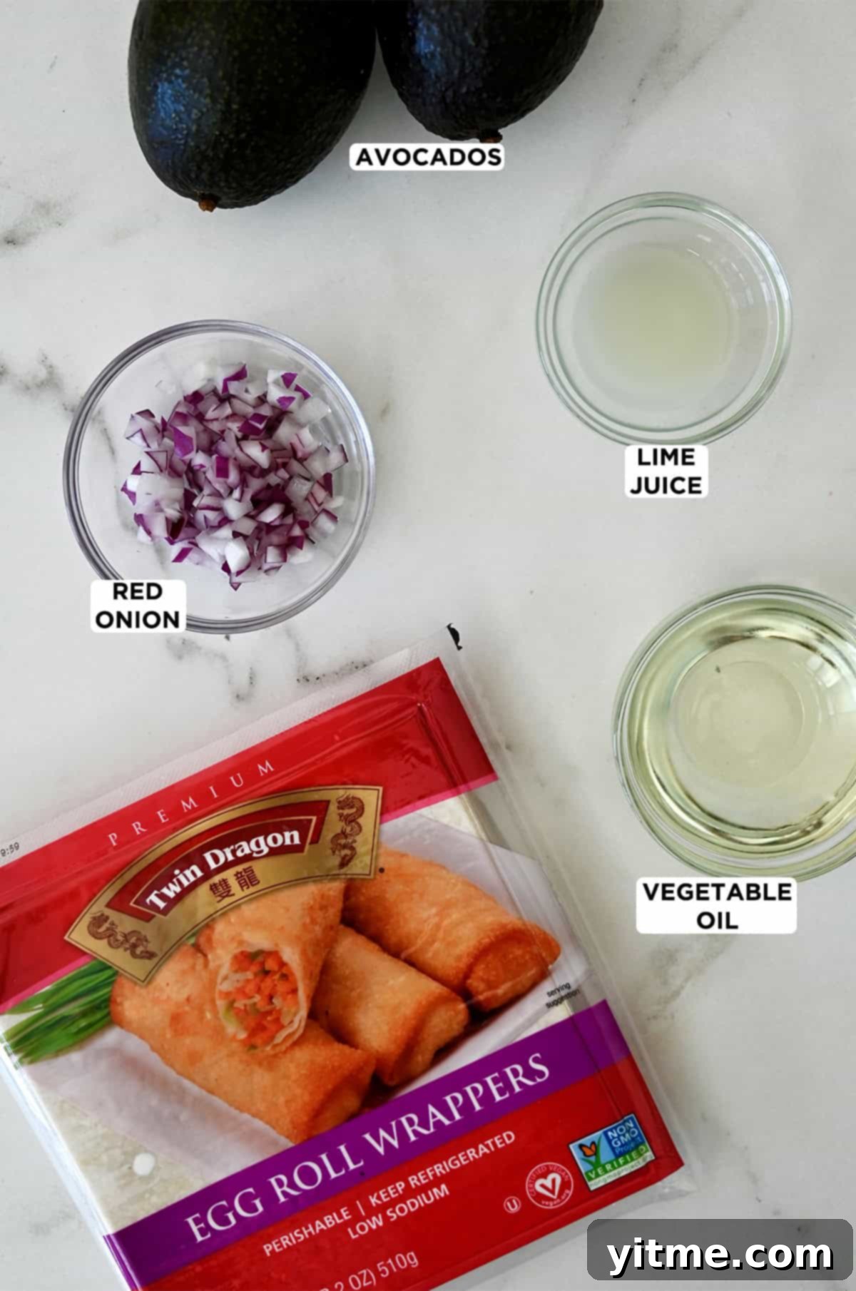 Egg roll wrappers next to glass bowls containing diced red onion, lime juice and vegetable oil, plus two ripe avocados.