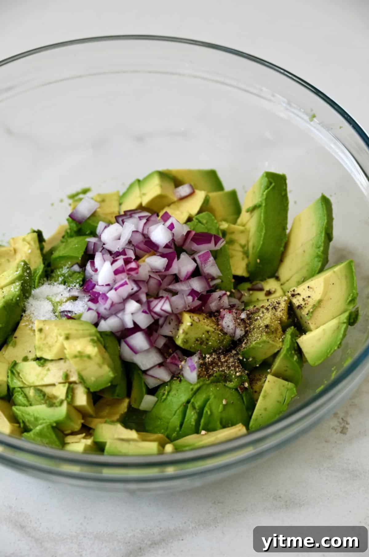 Diced red onions and avocado in a glass bowl.