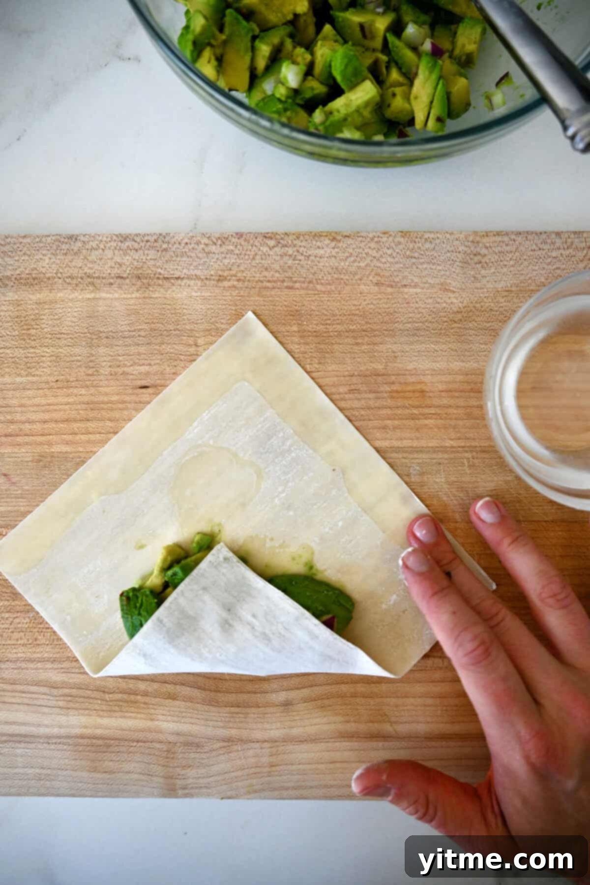 The first fold to making an egg roll, the bottom portion is folded over an avocado filling.