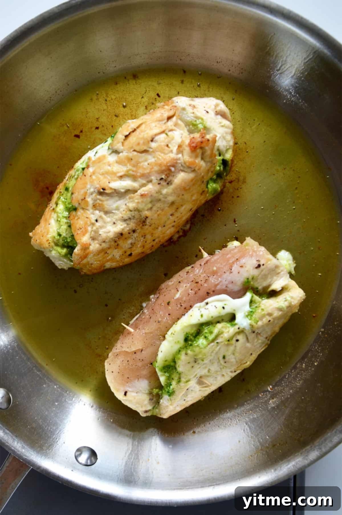 Pesto and mozzarella-stuffed chicken breasts are cooking in a skillet.