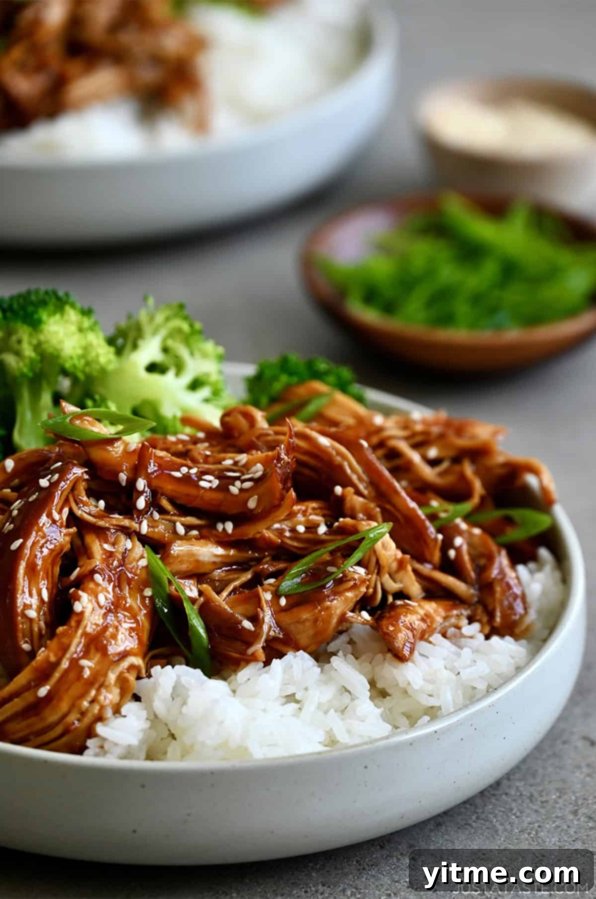 Slow cooker teriyaki chicken served over white rice in a bowl with steamed broccoli.