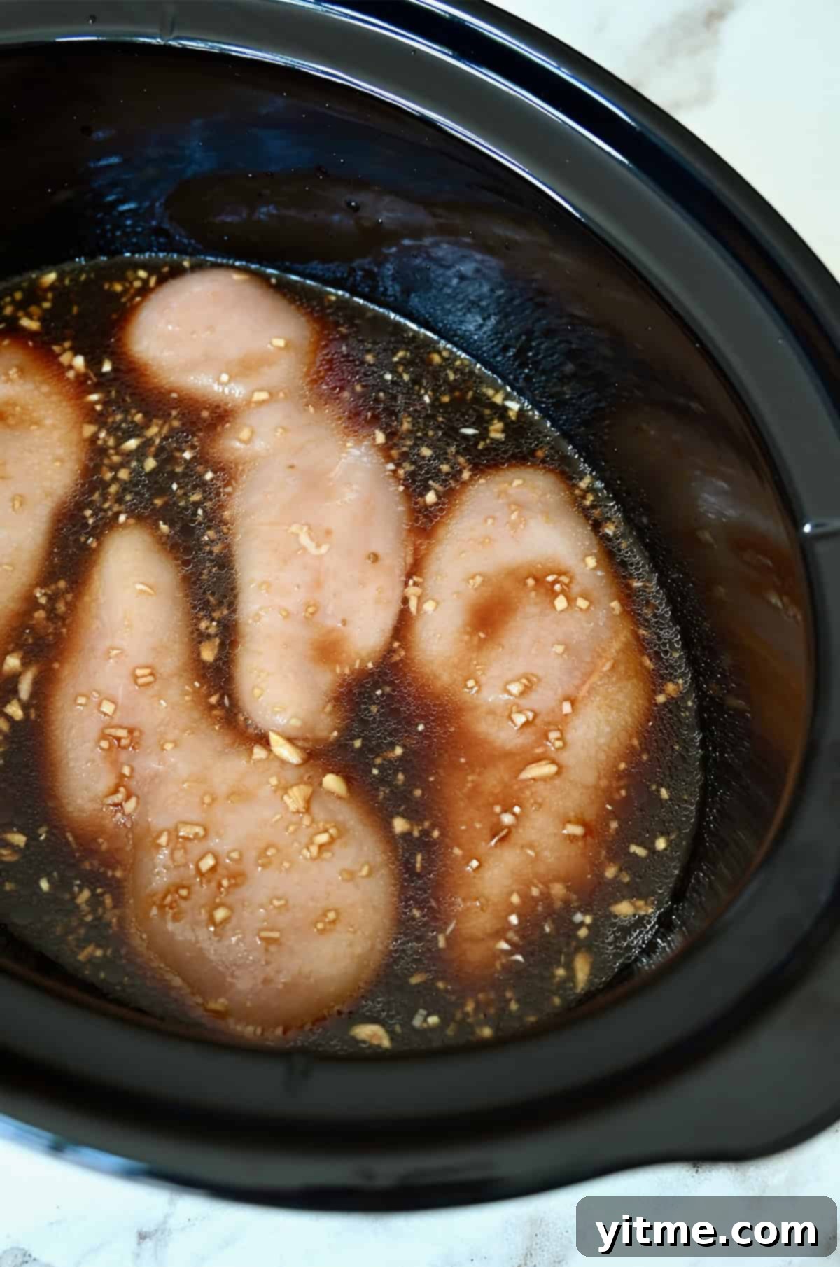 Raw chicken breasts in a slow cooker covered with a teriyaki marinade.