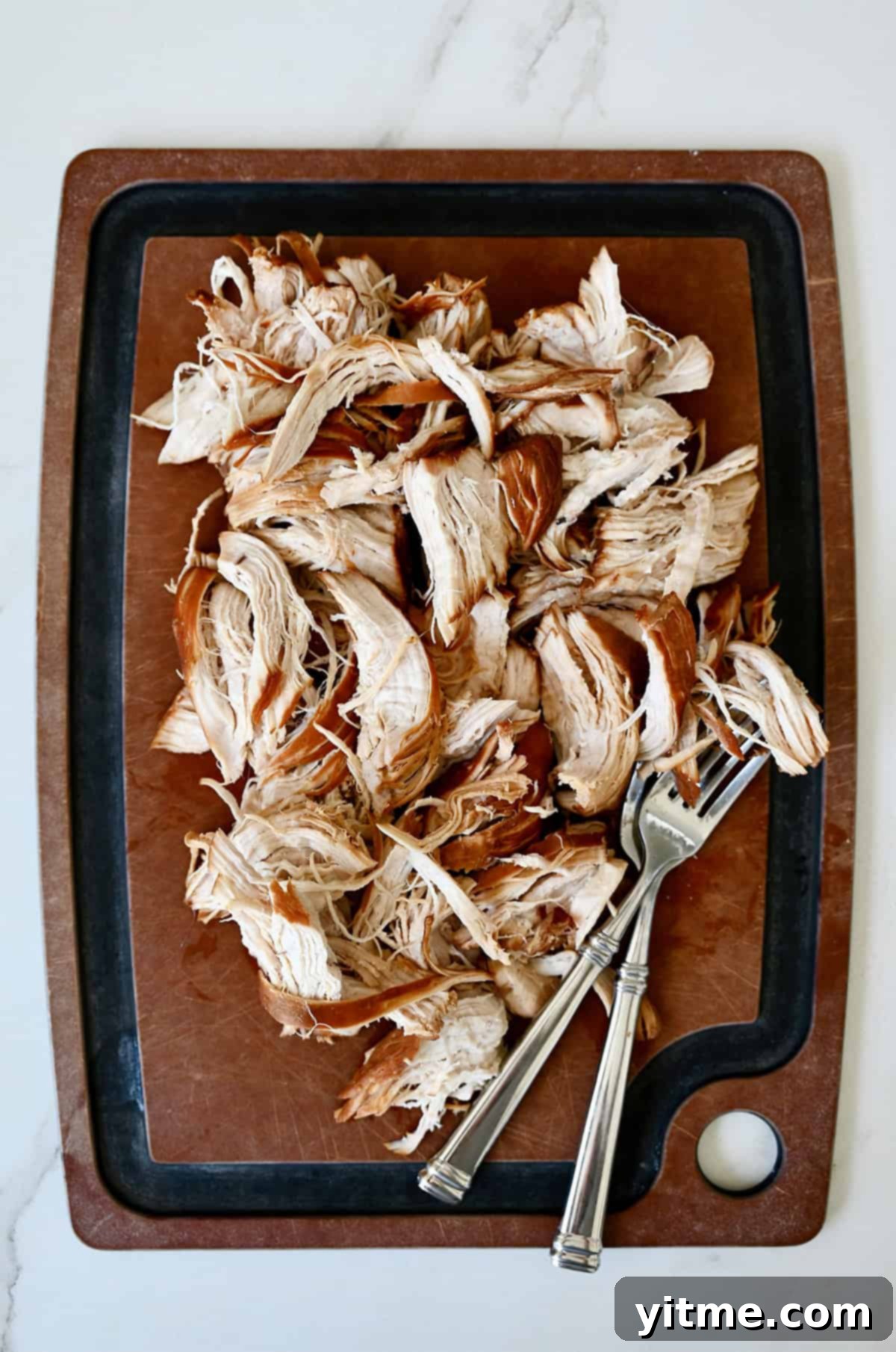 Shredded chicken with two forks on a cutting board.